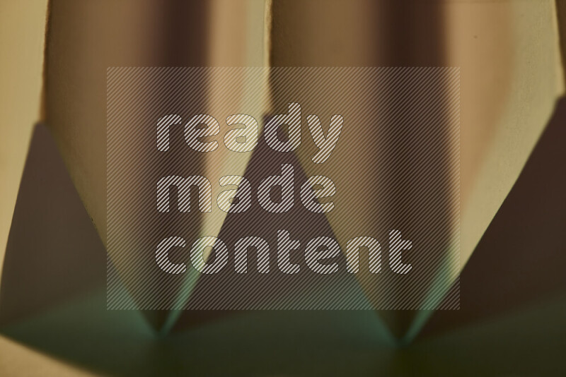 A close-up abstract image showing sharp geometric paper folds in green gradients and warm tones