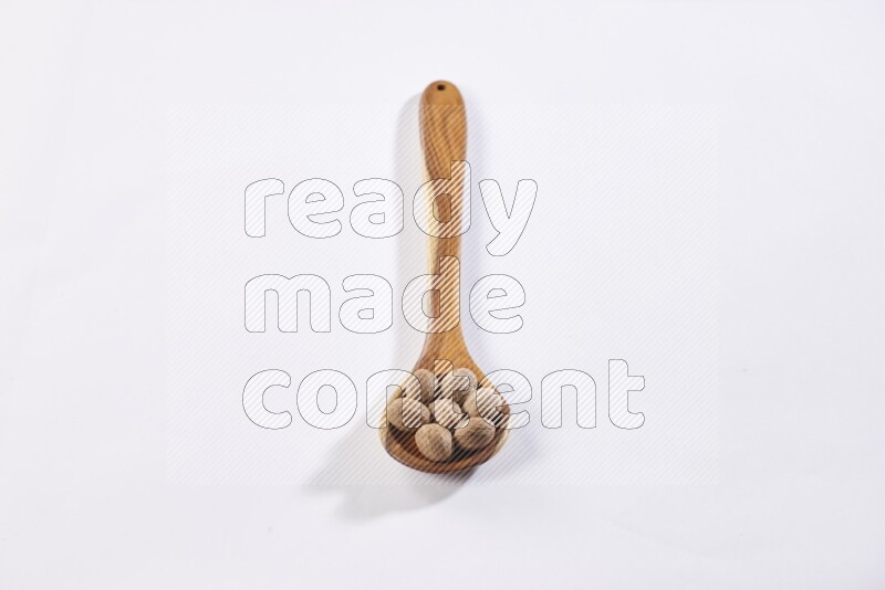 A wooden ladle full of whole nutmeg seeds on a white flooring