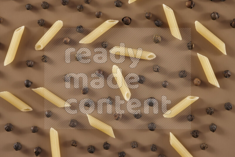 Raw pasta with different ingredients such as cherry tomatoes, garlic, onions, red chilis, black pepper, white pepper, bay laurel leaves, rosemary and cardamom on beige background