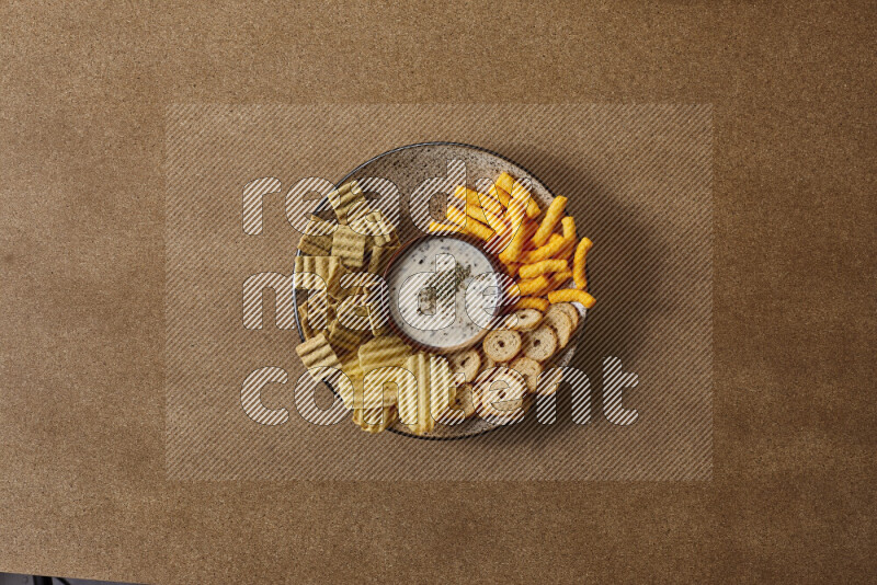 Assorted snacks on a pottery plate with a dipping on brown background