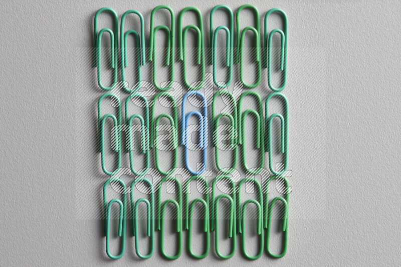 A bunch of green paper clips with a different colored paper clip in the center on grey background