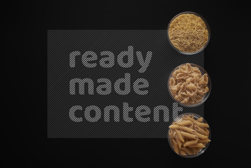 Different pasta types in 3 glass bowls on black background