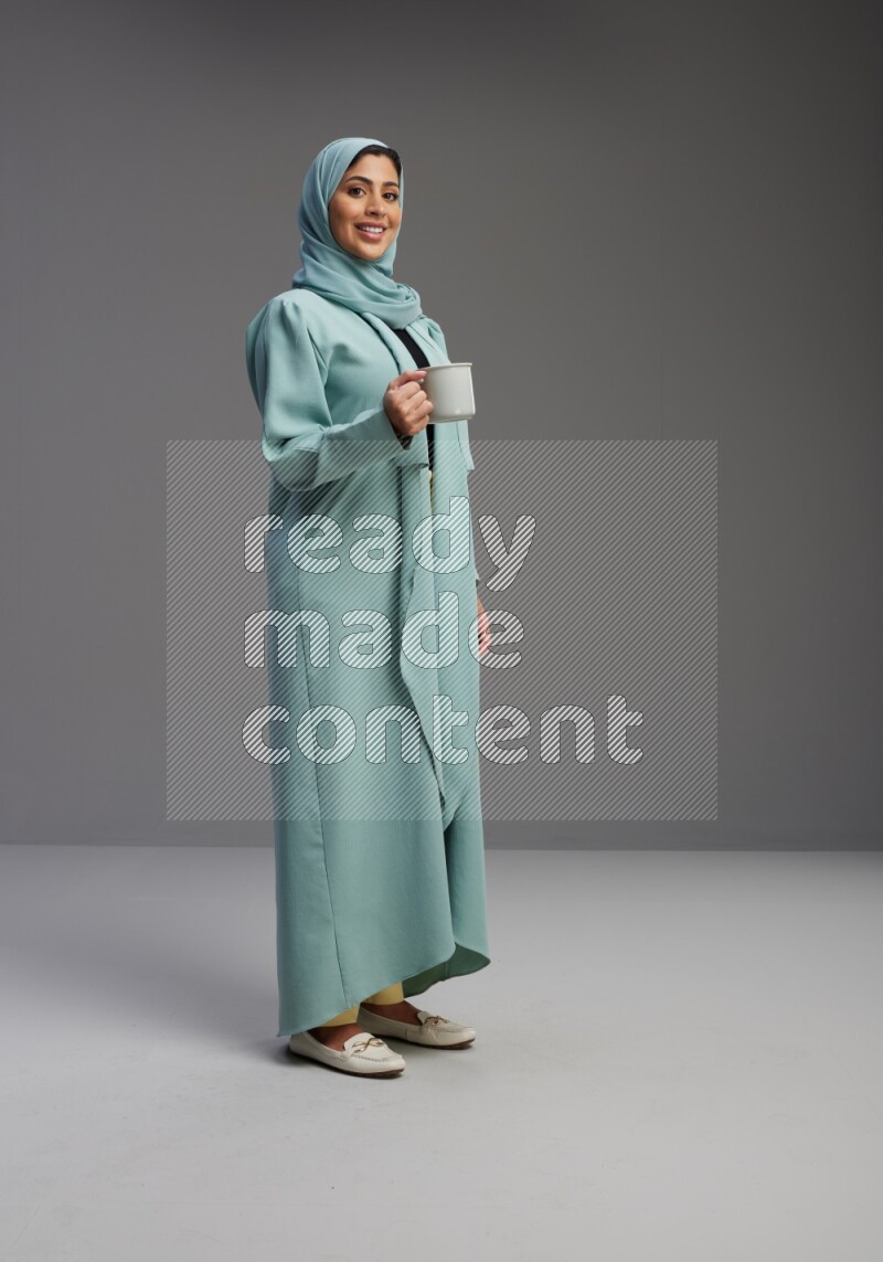 Saudi Woman wearing Abaya standing  holding a mug on Gray background