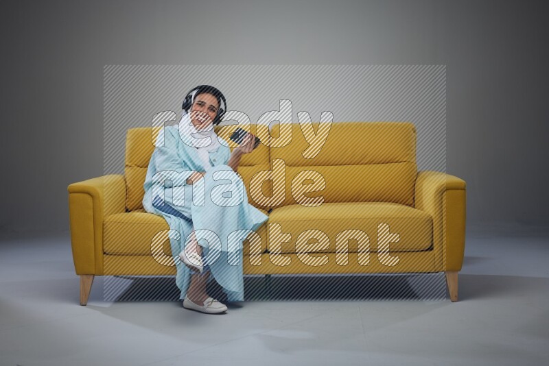 A Saudi woman sitting on a yellow Sofa Watching a Movie wearing Blue Abaya
