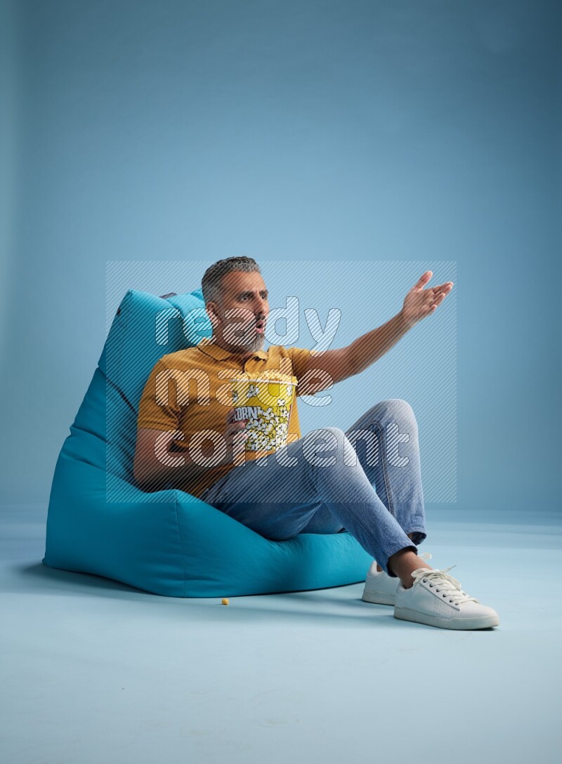 A man sitting on a blue beanbag and eating popcorn