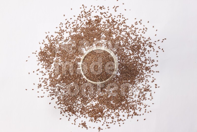 A pottery beige bowl full of flax seeds and more seeds spread on a white flooring