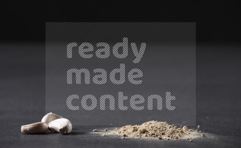 كومة صغيرة من بودرة الثوم مع بعض فصوص الثوم ورأس ثوم كاملة على خلفية سوداء