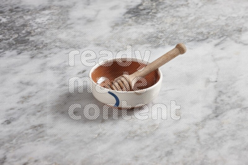 Multicolored pottery bowl with wooden honey dipper in it on grey marble background