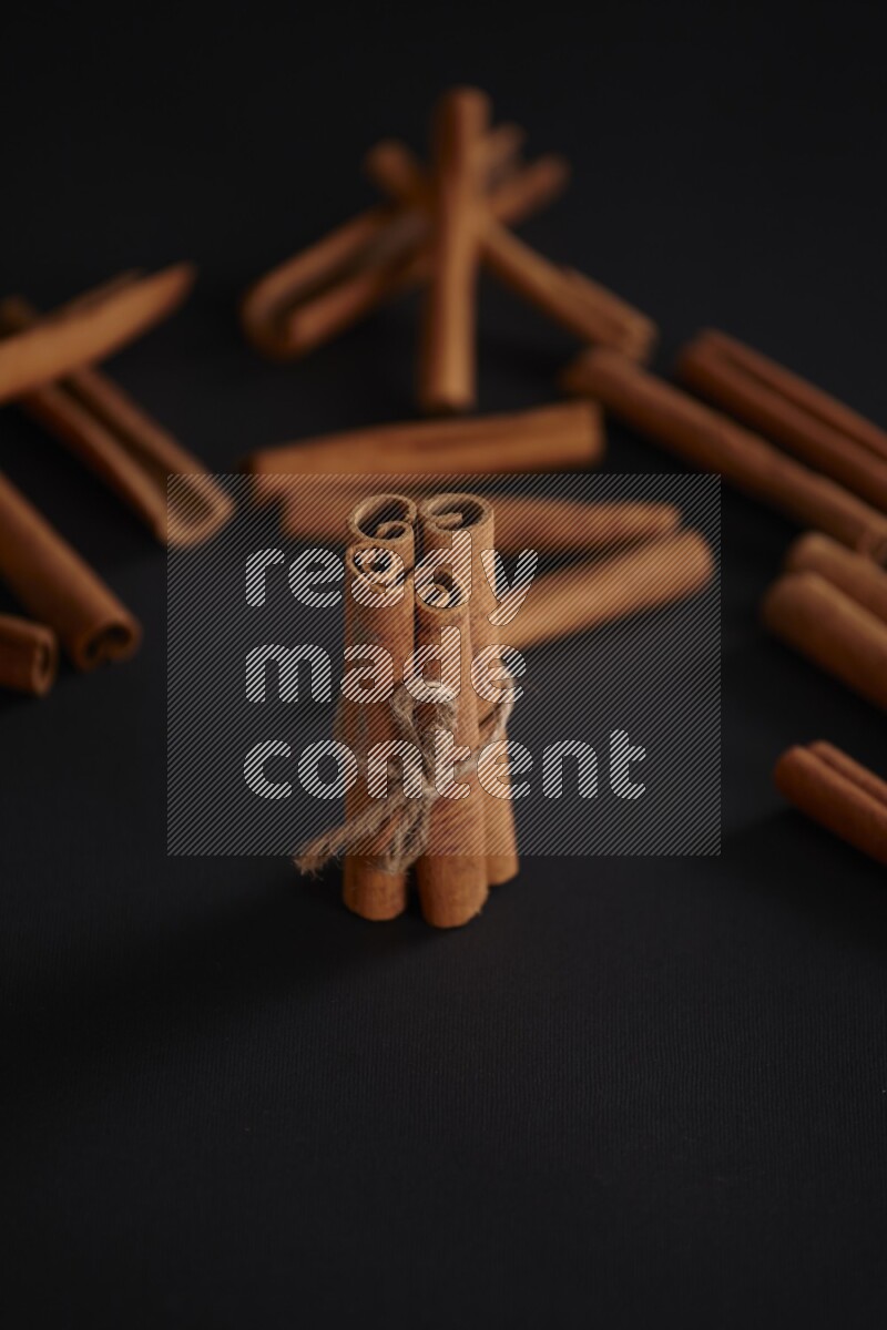 4 Cinnamon sticks stacked and bounded with more sticks in the background on black flooring
