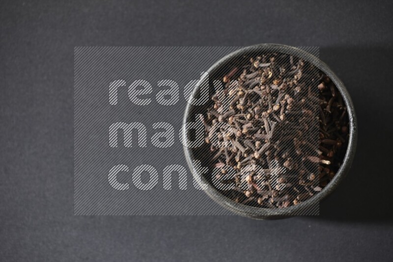 A black pottery bowl full of cloves on a black flooring