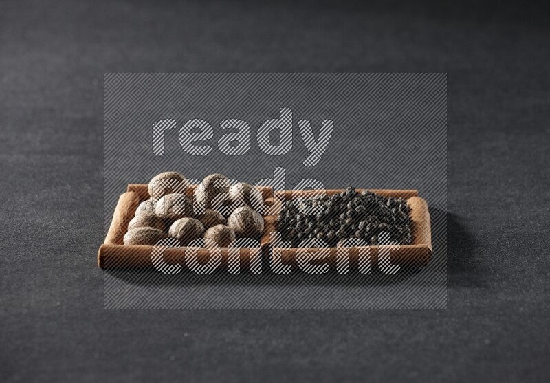 2 squares of cinnamon sticks full of nutmegs and black peppers on black flooring