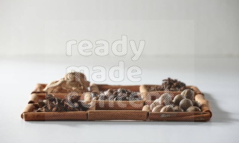 9 squares of cinnamon sticks full of coffee beans in the middle surrounded by dried mint, dried ginger, cardamom, star anise, cinnamon, nutmeg, dried basil and cloves on white flooring
