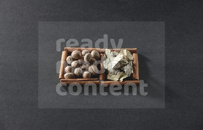 مربعان من أعواد القرفة ممتلئان بجوزة الطيب وأوراق الغار علي خلفية سوداء