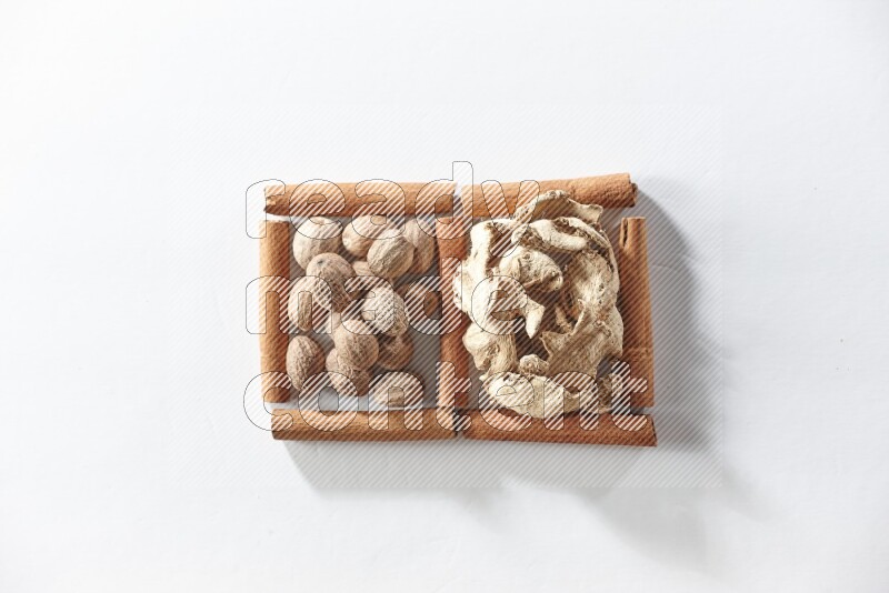 مربعان من أعواد القرفة ممتلئان بالزنجبيل المجفف وجوزة الطيب علي خلفية بيضاء