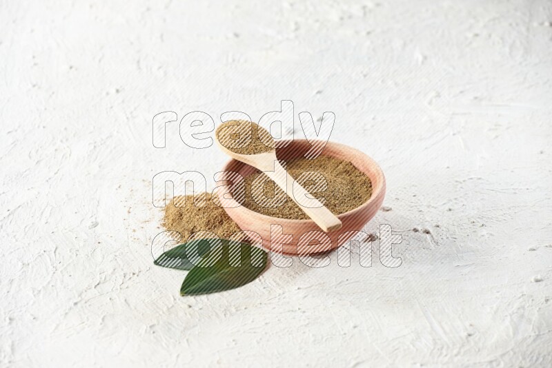A wooden bowl and wooden spoon full of cumin powder on textured white flooring