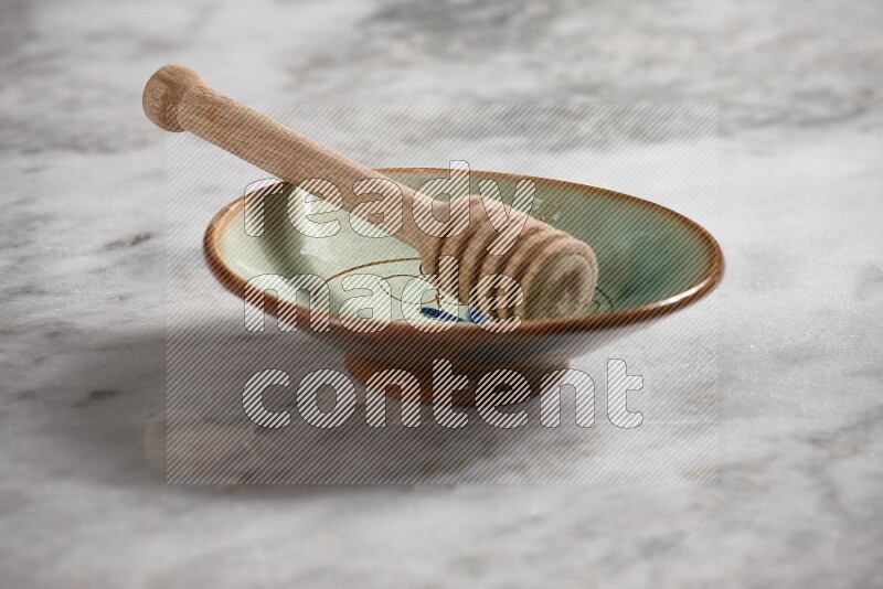 Decorative pottery plate with wooden honey dipper in it on grey marble background