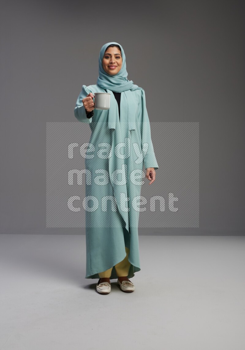 Saudi Woman wearing Abaya standing  holding a mug on Gray background