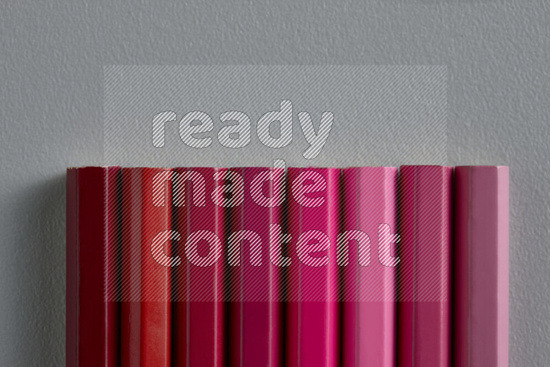 مجموعة من أقلام الرصاص الملونة مرتبة لتعرض تدرجا من اللون الوردي والأحمر علي خلفية رمادية