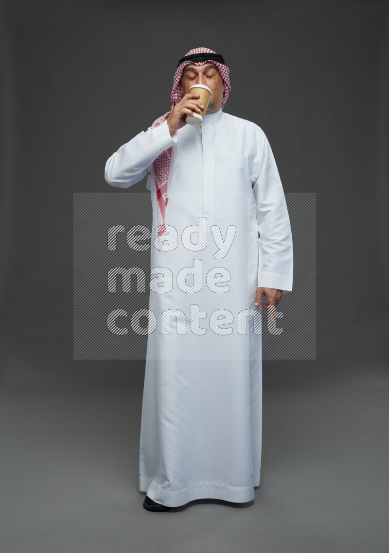 Saudi man with shomag Standing holding paper cup on gray background
