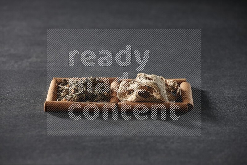 2 squares of cinnamon sticks full of dried ginger and dried basil on black flooring