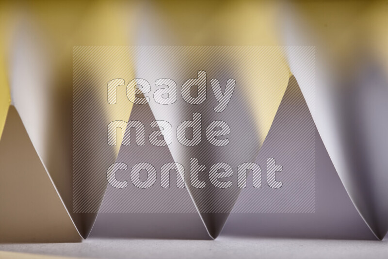 A close-up abstract image showing sharp geometric paper folds in white gradients and warm tones
