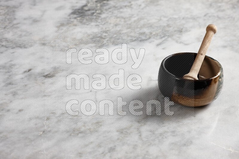 Multicolored pottery bowl with wooden honey dipper in it on grey marble background