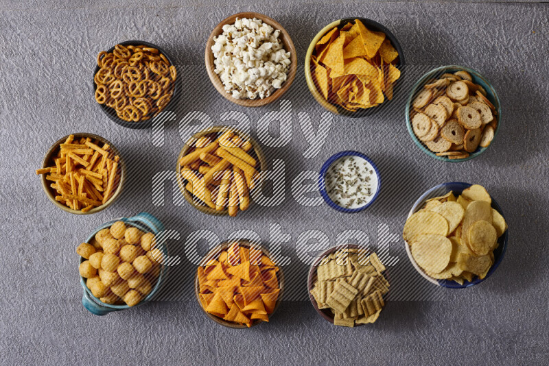 Assorted snacks in pottery bowls on grey background