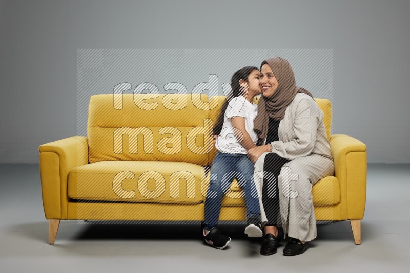 A girl with her mother sitting and interacting with the camera on gray background