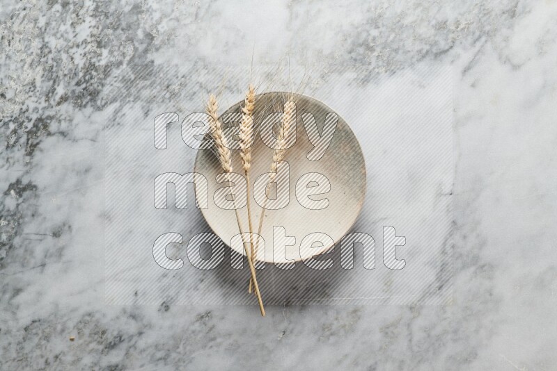 Wheat stalks on multicolored pottery plate on grey marble background