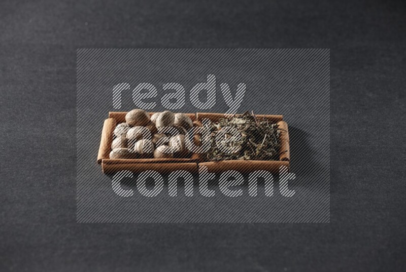 2 squares of cinnamon sticks full of nutmegs and dried basil on black flooring