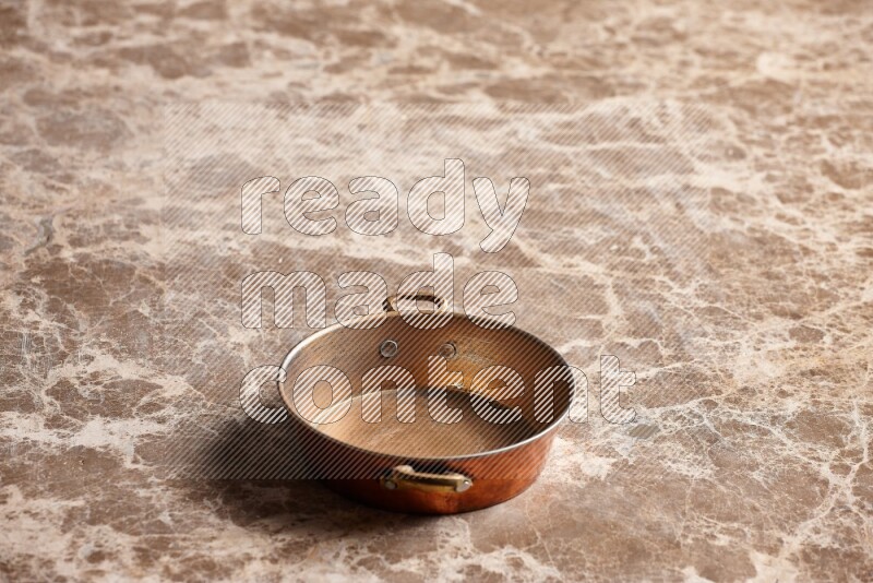 A small copper pan on beige marble background