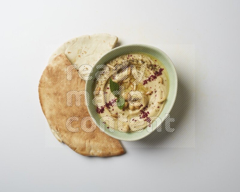 Hummus in a green plate garnished with zattar & sumak on a white background