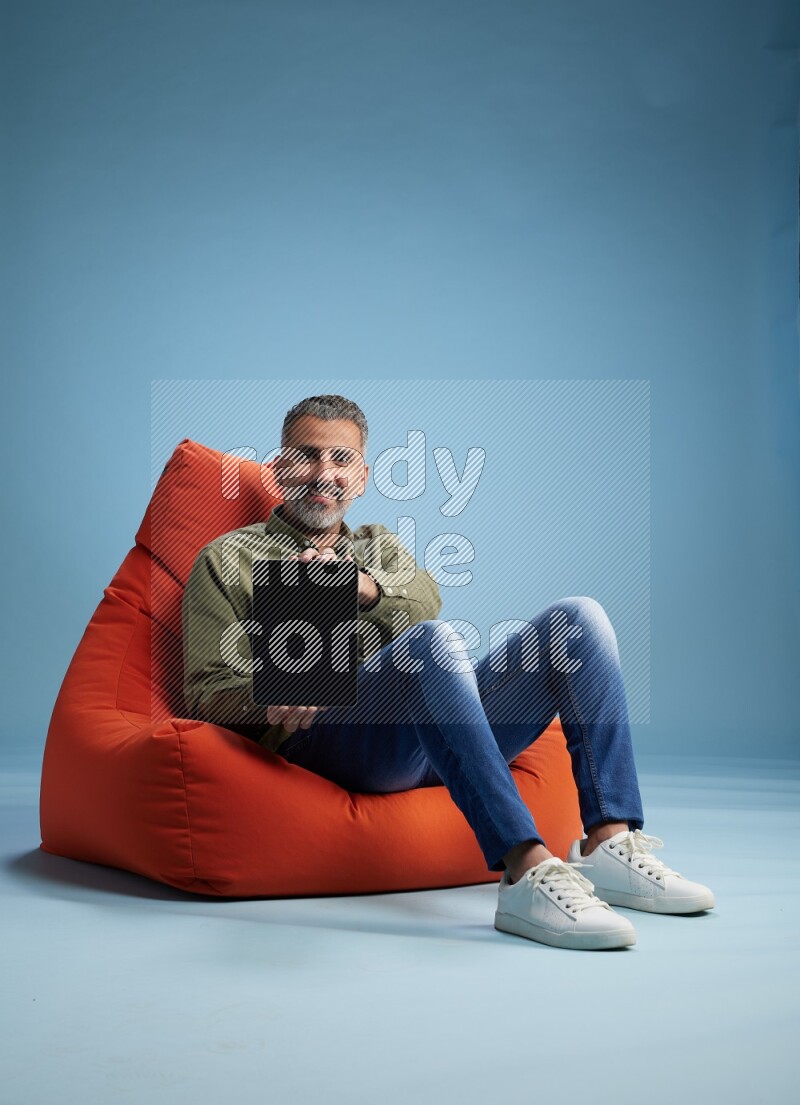 A man sitting on an orange beanbag and working on tablet