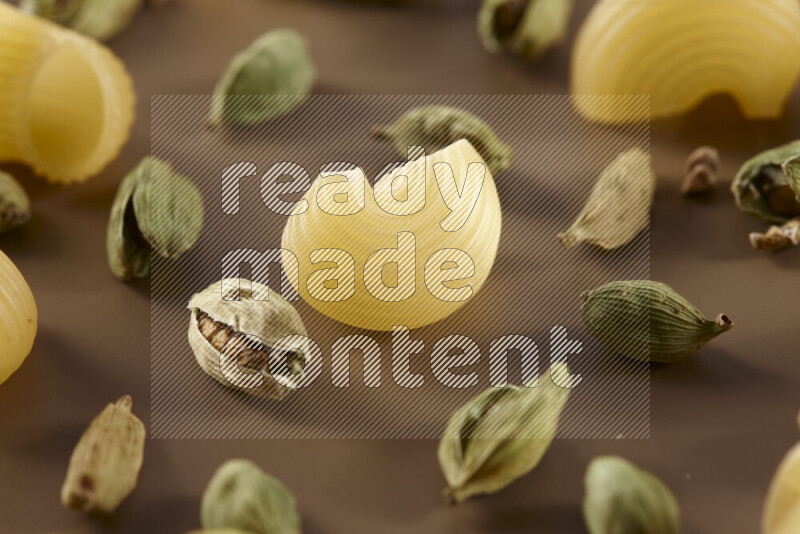 Raw pasta with different ingredients such as cherry tomatoes, garlic, onions, red chilis, black pepper, white pepper, bay laurel leaves, rosemary and cardamom on beige background