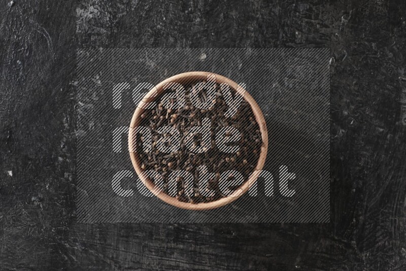 A wooden bowl full of cloves on a black flooring