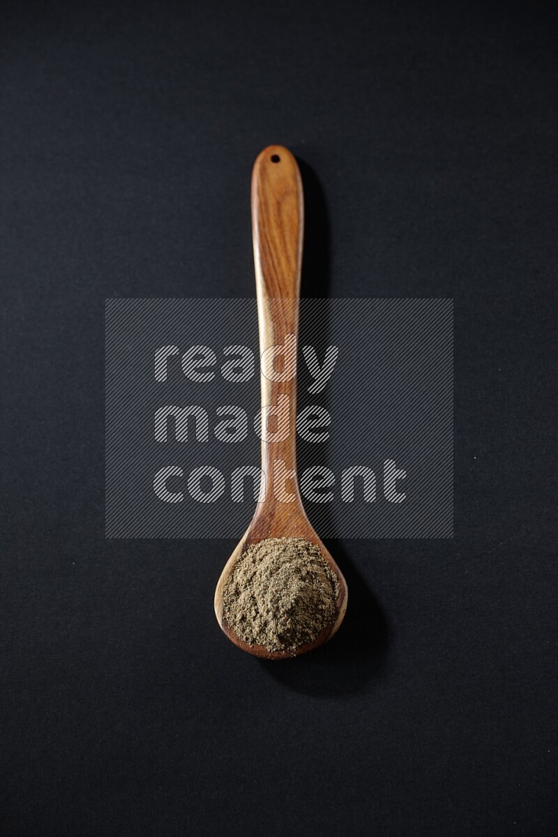 A wooden ladle full of cardamom powder on black flooring