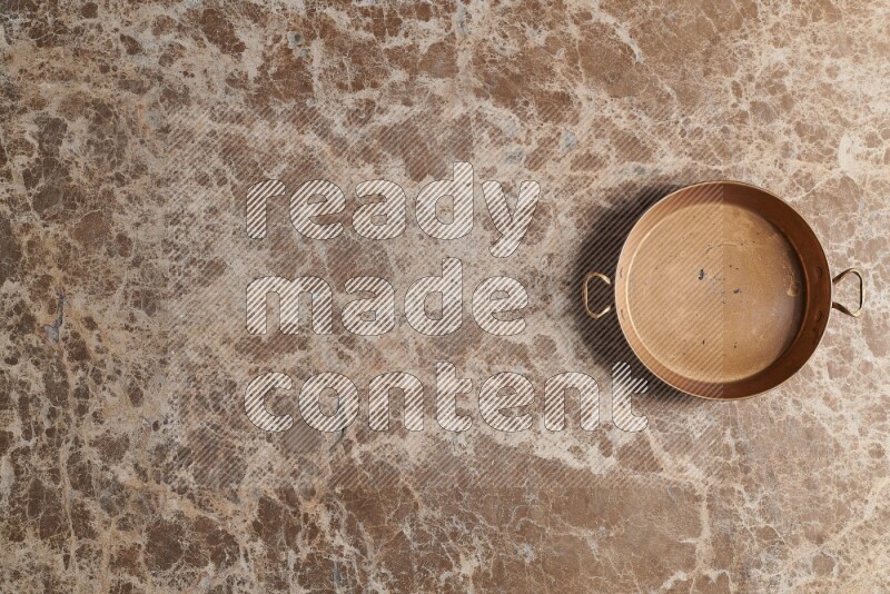 A small copper pan on beige marble background