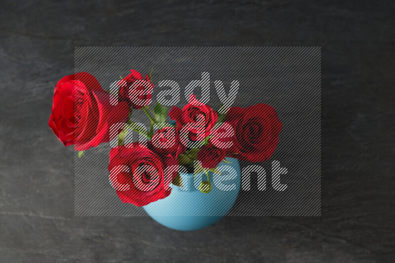 An arrangement of vivid red roses in a blue vase on black marble background