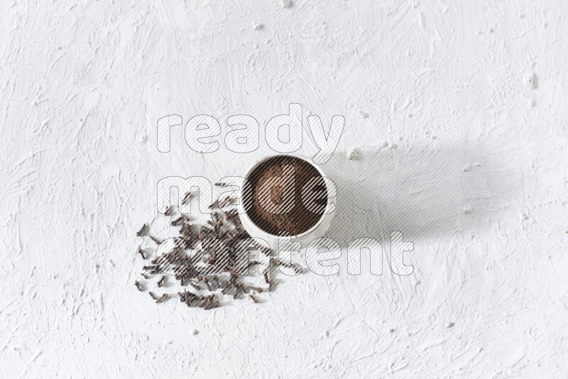 A beige ceramic bowl full of cloves powder and whole cloves on a white flooring