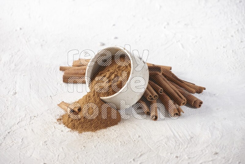 Ceramic beige bowl over filled with cinnamon powder and cinnamon sticks around the bowl on a textured white background in different angles