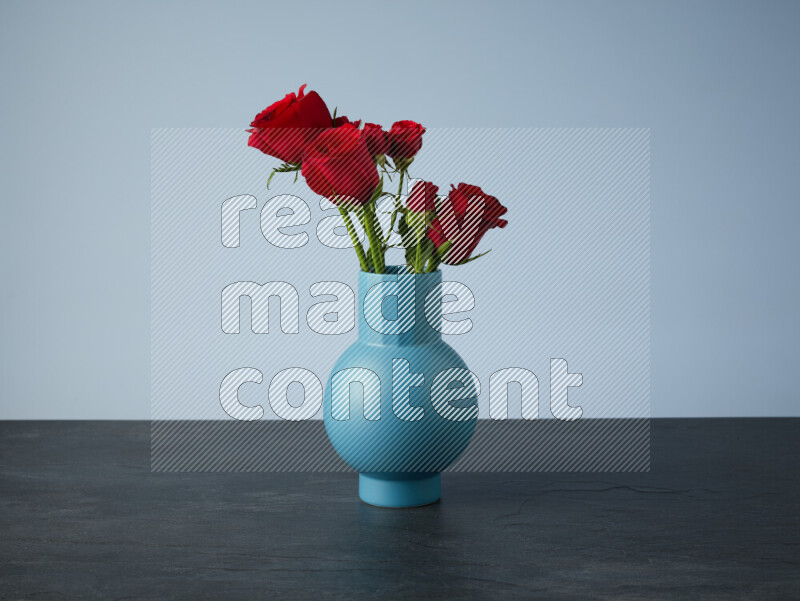 An arrangement of vivid red roses in a blue vase on black marble background