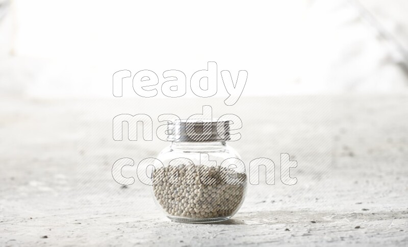 Herbal Glass jar full of white pepper beads on textured white flooring