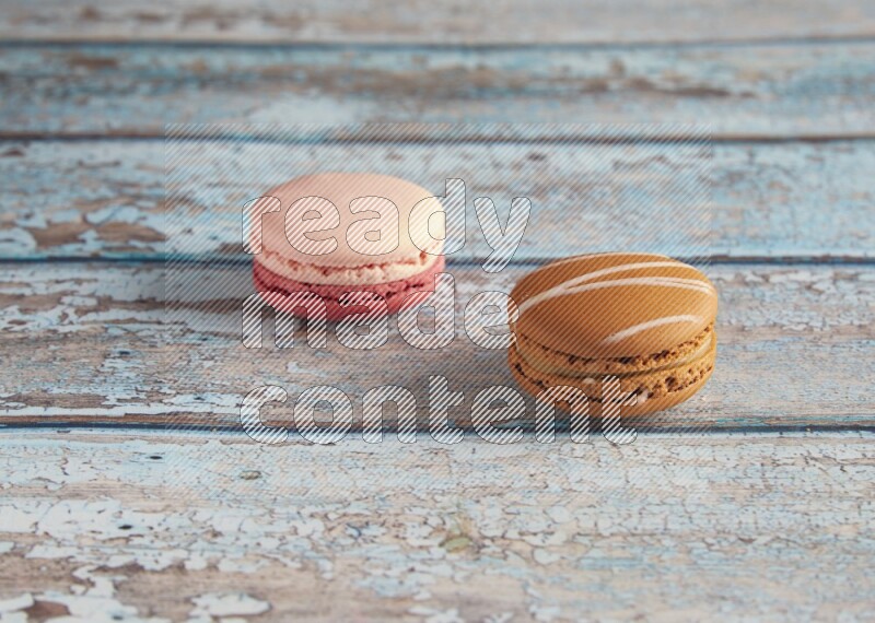 45º Shot of of two assorted Brown Irish Cream, and Pink Litchi Raspberry macarons on light blue background