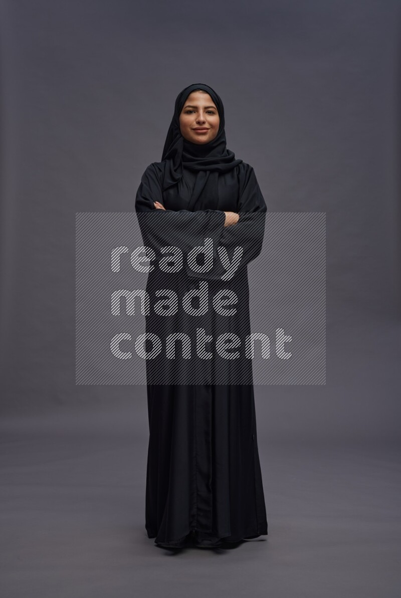 Saudi woman wearing Abaya standing with crossed arms on gray background