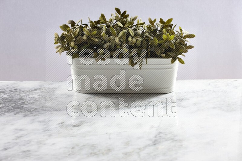 Multiple green artificial plants in white pot on grey marble background