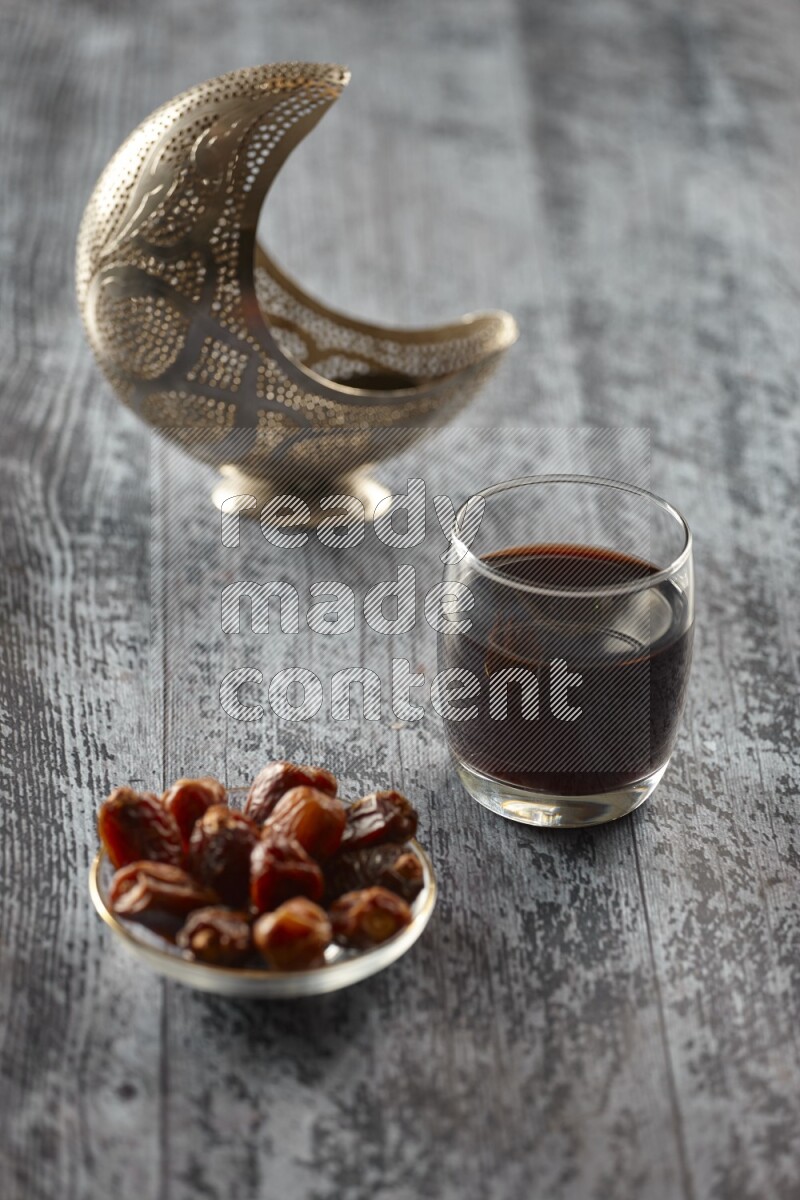 A silver lantern with different drinks, dates, nuts, prayer beads and quran on grey wooden background