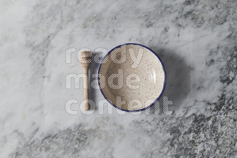 وعاء فخاري متعدد الألوان مع ملعقة عسل خشبية بجانبه على خلفية رخام رمادي