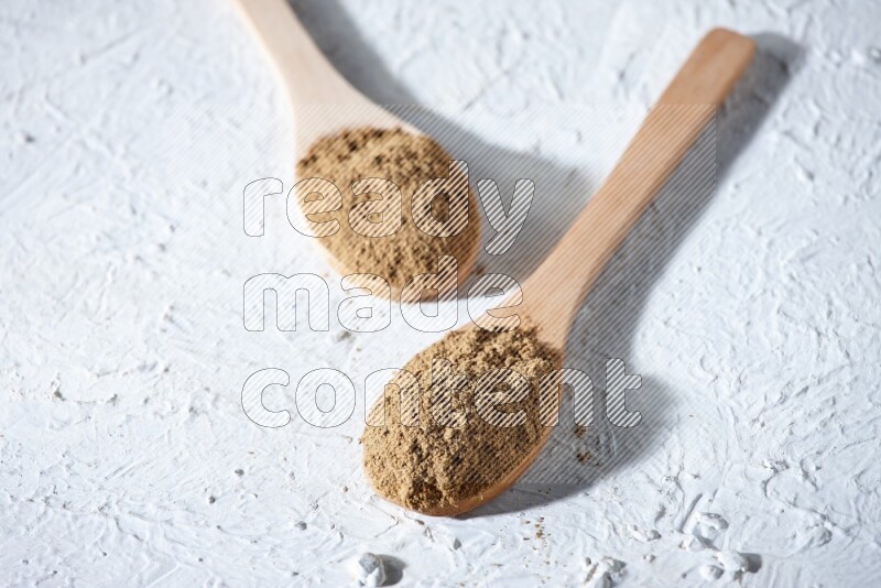 Wooden spoons full of allspice powder and allspice whole balls spreaded on a textured white flooring