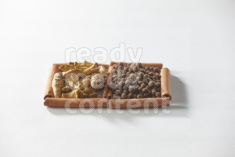 مربعان من أعواد القرفة ممتلئان ببهار الفلفل الحلو وأصابع الكركم علي خلفية بيضاء