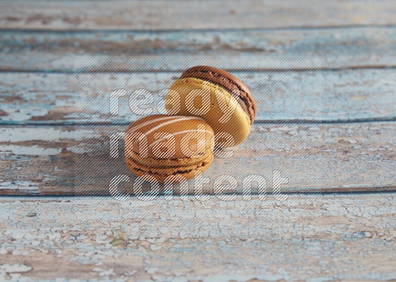 45º Shot of of two assorted Brown Irish Cream, and Yellow, and Brown Chai Latte macarons  on light blue background